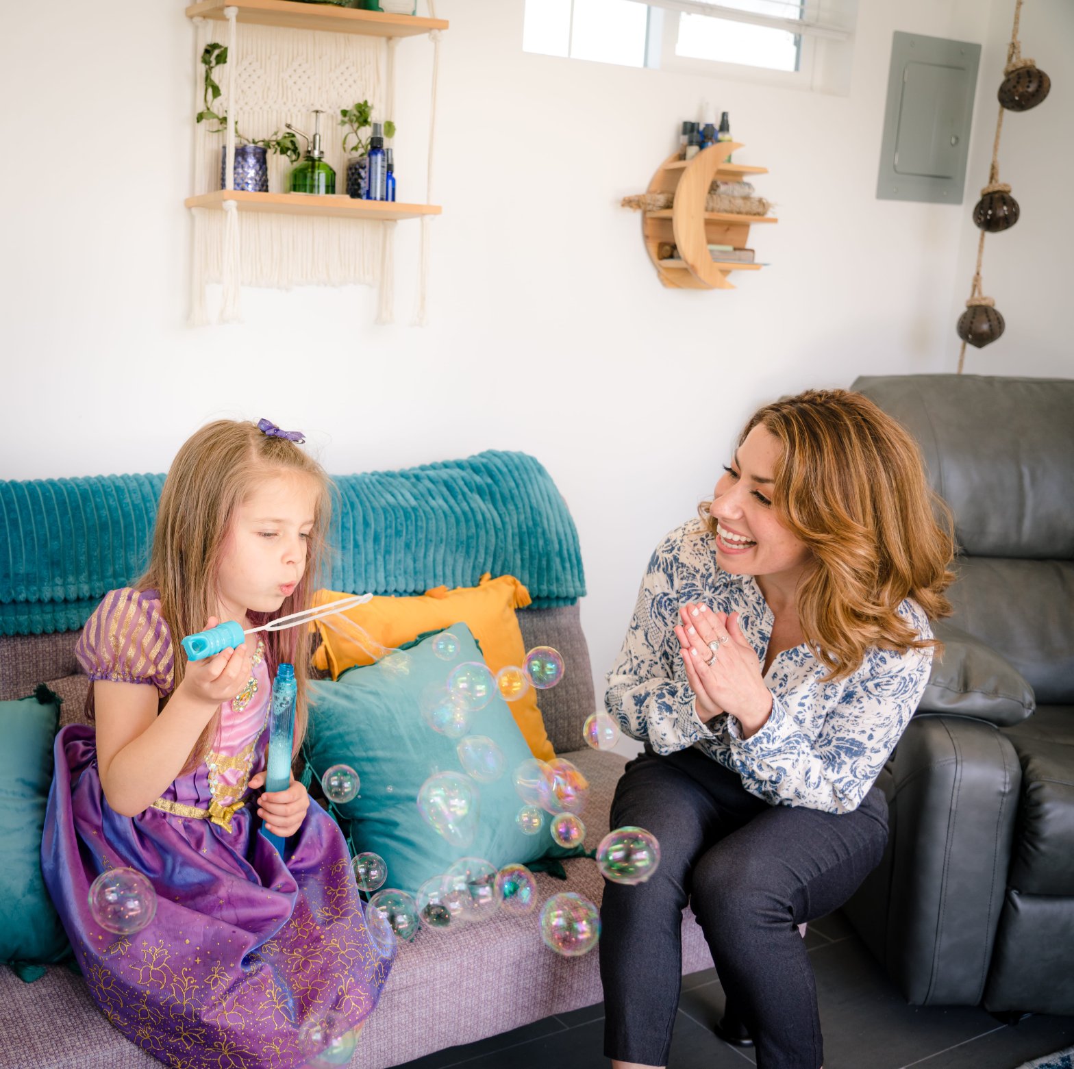 Meredith smiling beside a young client blowing soap bubbles in the calming session room