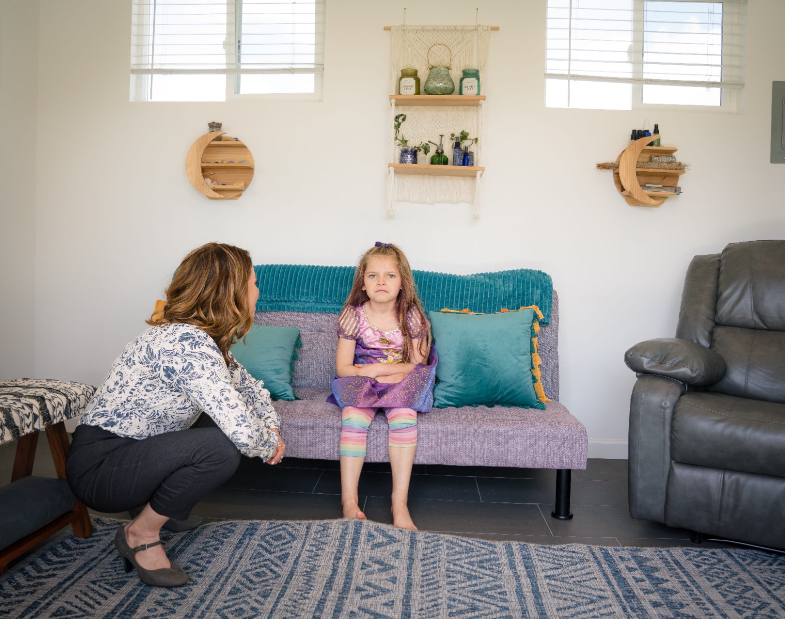 Meredith crouching to eye level beside a young client seated on the session sofa